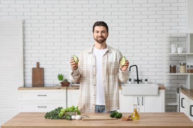 Mutfaktaki ahşap masada taze avokadosu ve sağlıklı yiyeceği olan sakallı genç bir adam.