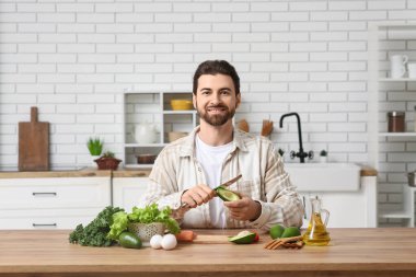 Avokado soyan sakallı genç bir adam ve mutfak masasında sağlıklı yiyecekler.