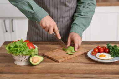 Tahta masada kahvaltıda taze avokado kesen adam.