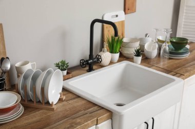 Seramik lavabo, temiz tabak ve gri duvarın yanındaki ahşap mutfak tezgahına bitkiler.