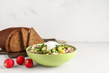 Bir kase lezzetli okroshka, ekşi krema, ekmek ve açık arkaplanda taze turp.