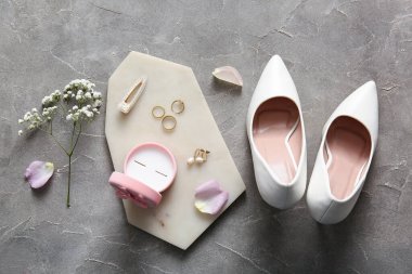 Mücevherli alyanslar, kutu, yüksek topuklu ayakkabılar ve gri arka planda çiçekler. Üst görünüm