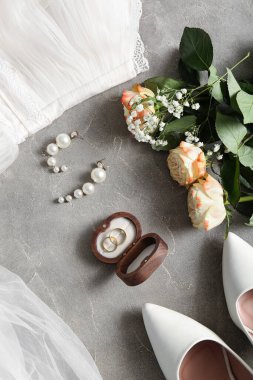 Tahta kutuda alyanslar, küpeler, çiçekler ve gri arka planda yüksek topuklar. Üst görünüm