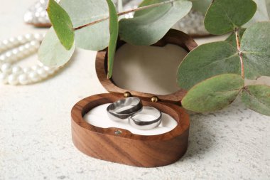 Beyaz arka planda okaliptüs dalı olan ahşap kutuda gümüş alyanslar.