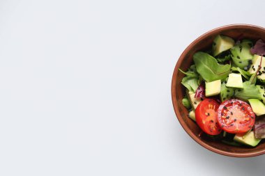 Bir kase lezzetli avokado salatası, vişneli domates ve gri arka planda susam tohumları.