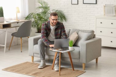 Oturma odasında kanepede otururken laptop kullanan yakışıklı adam.