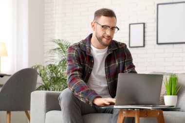 Oturma odasında kanepede otururken laptop kullanan yakışıklı adam.