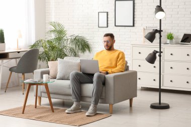 Evde kanepede dizüstü bilgisayar kullanan genç adam