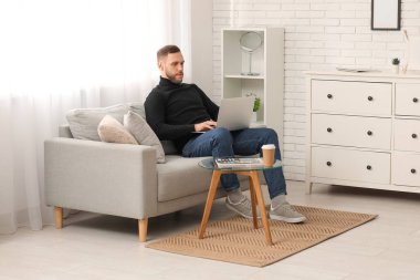 Evdeki kanepede dizüstü bilgisayarı olan genç bir serbest yazar.