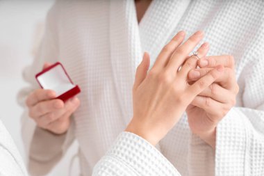 Genç adam yatak odasında kız arkadaşının parmağına nişan yüzüğü takıyor.