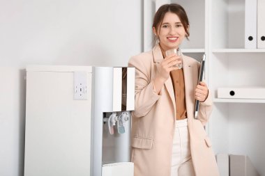 Güzel genç bayan ofisteki soğutucudan su içiyor.