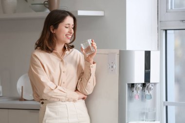 Mutfaktaki soğutucudan su içen gülümseyen genç kadın.