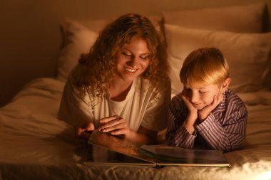 Genç anne, çocuğu için evde kitap okuyor.