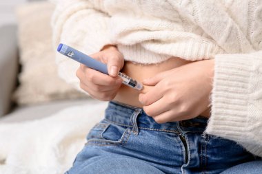 Diyabet hastası genç bir kadın evde kendine insülin iğnesi yapıyor.