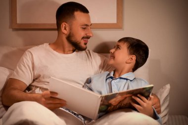 Baba ve küçük oğlu yatakta masal okuyorlar.