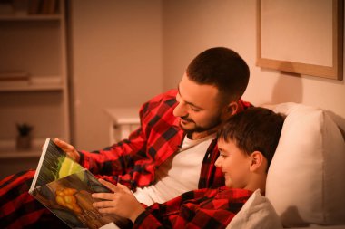 Genç baba, çocuğuna evde masal okuyor.