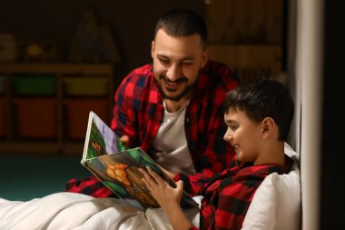 Baba ve küçük oğlu evde birlikte kitap okuyorlar.