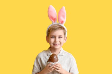 Çikolata yumurtası ve sarı arka planda tavşan kulaklı küçük bir çocuk.