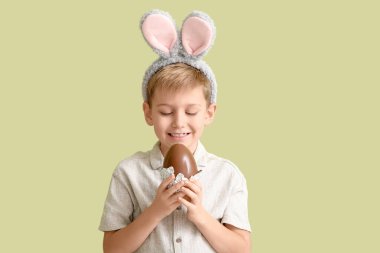 Çikolata yumurtası ve yeşil arka planda tavşan kulaklı küçük bir çocuk.