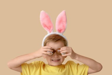 Çikolata yumurtası ve bej arka planda tavşan kulaklı küçük bir çocuk.