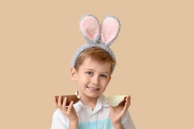 Çikolata yumurtası ve bej arka planda tavşan kulaklı şirin bir çocuk.