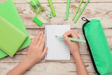 Çocuğun elleri kağıda beyaz ahşap arka plana bir şeyler yazıyor. Üst görünüm