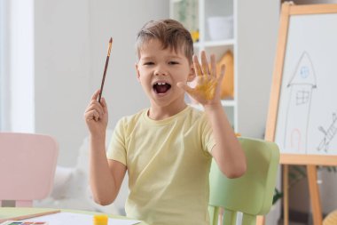 Oturma odasındaki masada eli boyalı küçük mutlu çocuk.