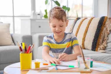 Keçeli kalemlerle evde çizim yapan gülümseyen küçük çocuk.