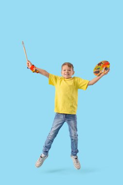 Mavi arka planda boya paleti ve fırçası olan küçük çocuk.