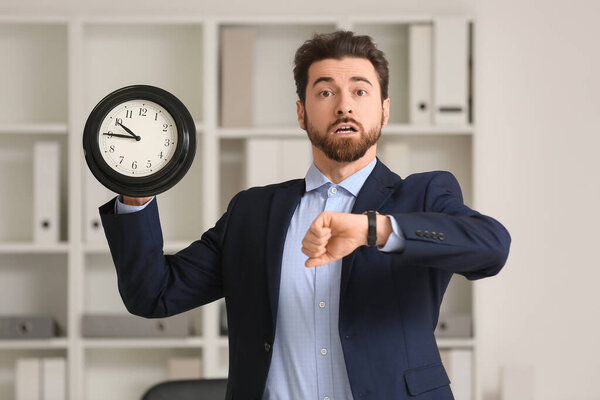 Стрессовый бизнесмен смотрит на часы и держит часы в офисе, концепция крайнего срока
