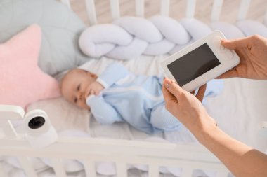 Anne, beşiğinde bebeğinin yanında bebek telsizi tutuyor.