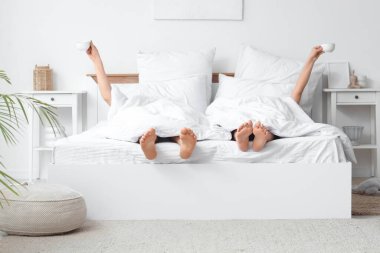 Yatak odasında battaniyenin altında kahve içen genç bir çift.