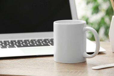 Ofisteki dizüstü bilgisayarın yanındaki masada seramik bardak.