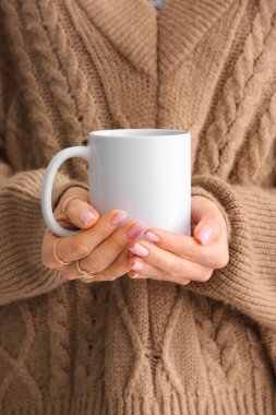 Elinde seramik bardak tutan sıcak kahverengi kazaklı bir kadın. Yakın çekim.