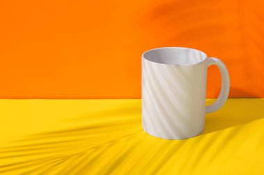 Sarı masada, turuncu duvara karşı, palmiye gölgesinde seramik bardak.