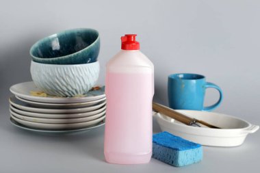 Kirli tabaklar, deterjan ve gri arka planda sünger.