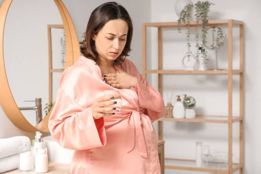 Pregnant woman with glass of water feeling unwell in bathroom clipart