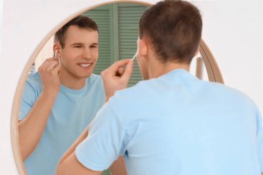 Genç adam aynanın yanında pamuk tomurcuklarıyla kulakları temizliyor.