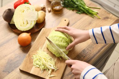 Mutfakta leziz borş çorbası için tahta tahtada lahana doğrayan genç bir kadın. Yakın çekim.