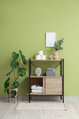 Tuvalet kağıdı ruloları ve vazolar yeşil duvarın yanındaki raf ünitesinde.