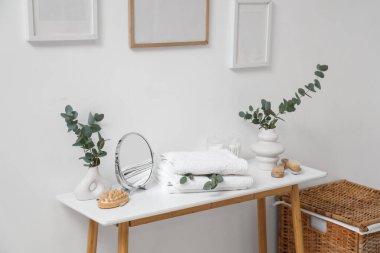 Okaliptüs dallı vazolar, ayna ve havlular banyodaki masada.