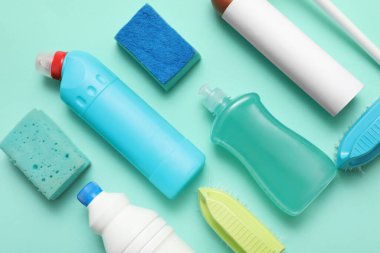 Turkuaz arka planda fırça ve süngerli deterjan şişeleri