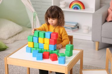 Oturma odasındaki masada plastik küplerle oynayan sevimli küçük kız.