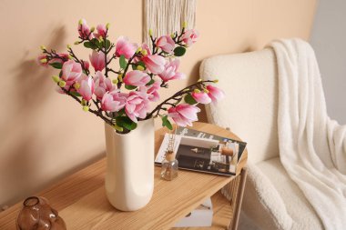 Oturma odasındaki şık koltuğun yanındaki konsol masasında çiçek açan vazo.