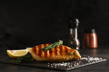 Lezzetli ızgara tavuk göğsü, limon dilimleri ve siyah grunge masasında biberiye.