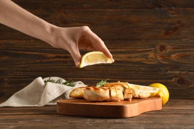 Limon sıkan bir kadın ızgara tavuk göğsünde biberiye ve ahşap arka planda biberli mısır.