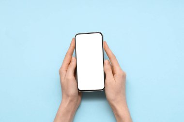 Mavi arka planda cep telefonu olan bir kadın el.