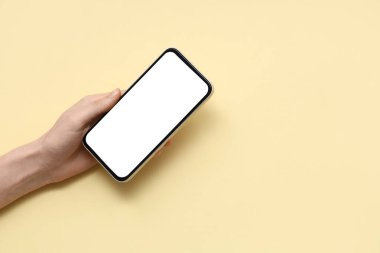 Female hand with mobile phone on yellow background