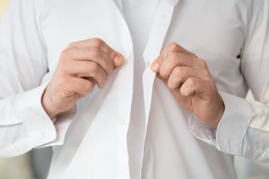 Genç adam şık beyaz gömleğini ilikliyor, yakın plan.