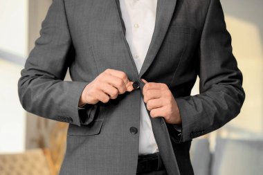 Genç adam evde şık bir takım elbise ilikliyor, yakın plan.